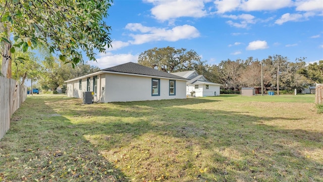 view of property exterior featuring cooling unit, stucco siding, a lawn, and fence