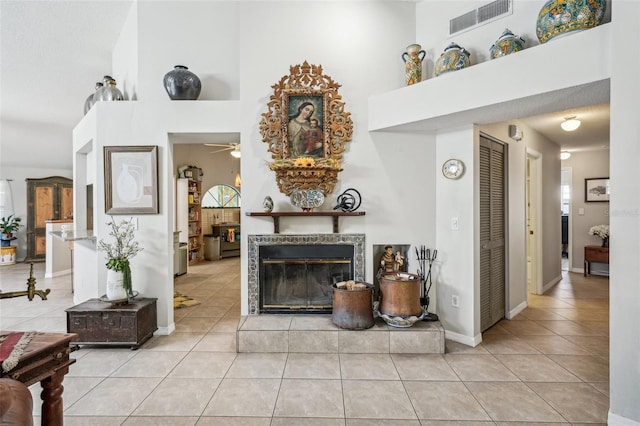 tiled living room featuring a tile fireplace, visible vents, a towering ceiling, and baseboards