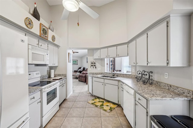 kitchen with white appliances, light tile patterned floors, a towering ceiling, ceiling fan, and a sink