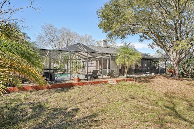 back of house with an outdoor pool, a yard, a chimney, and a lanai