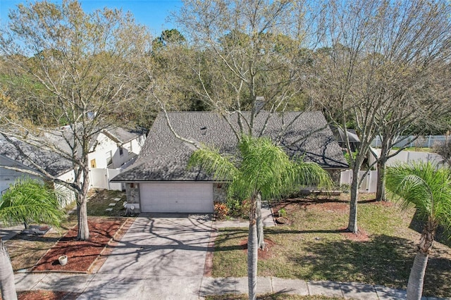 view of front of house featuring a garage, fence, stone siding, driveway, and roof with shingles