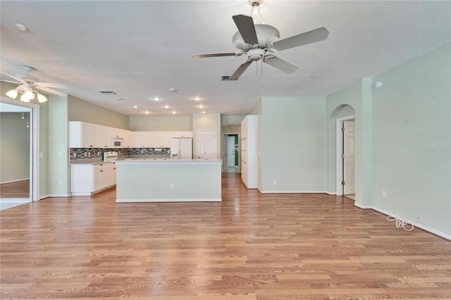 kitchen featuring white appliances, light wood finished floors, white cabinets, open floor plan, and backsplash