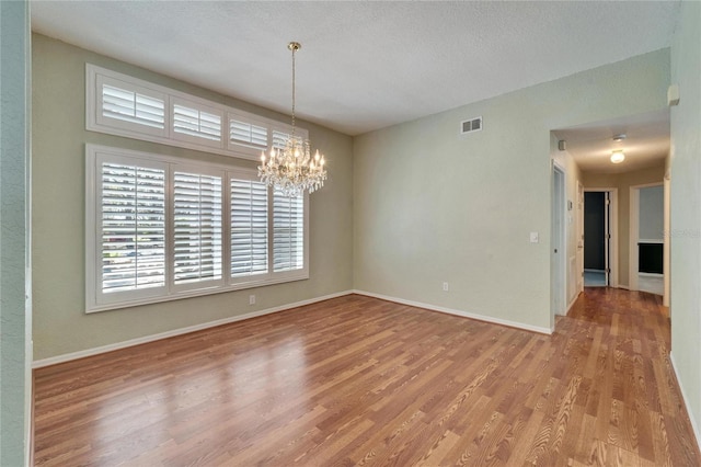 empty room with a chandelier, wood finished floors, visible vents, and baseboards