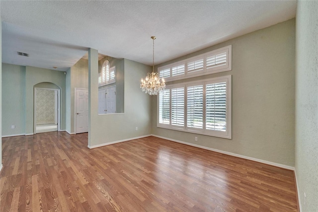 empty room featuring baseboards, visible vents, wood finished floors, a textured ceiling, and a notable chandelier