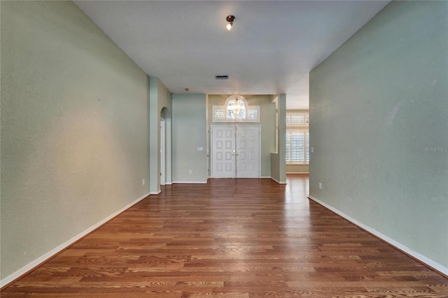 empty room with arched walkways, wood finished floors, visible vents, and baseboards