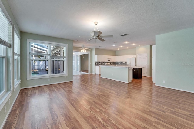 unfurnished living room featuring visible vents, a ceiling fan, a textured ceiling, wood finished floors, and baseboards