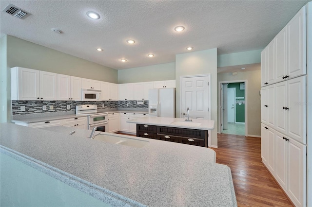 kitchen with white appliances, visible vents, a kitchen island, a sink, and backsplash