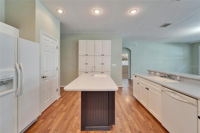 kitchen featuring arched walkways, white appliances, white cabinetry, and a sink