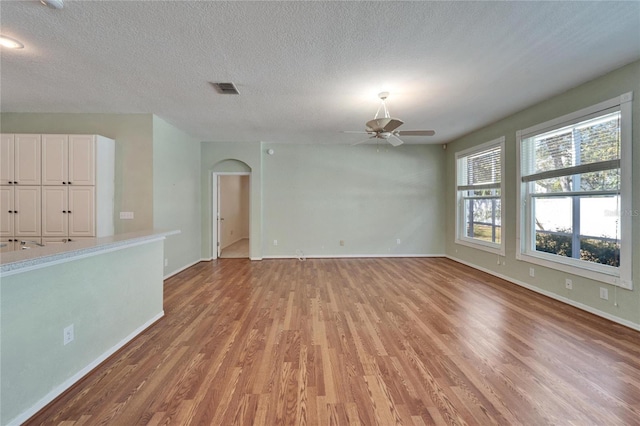 unfurnished living room with arched walkways, light wood finished floors, visible vents, a textured ceiling, and baseboards