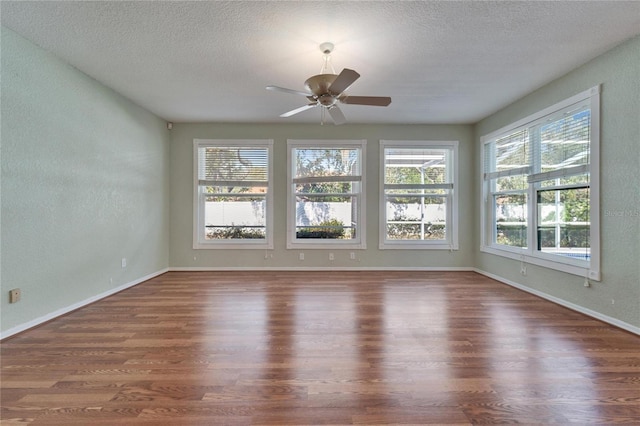 spare room with a healthy amount of sunlight, a textured ceiling, baseboards, and wood finished floors