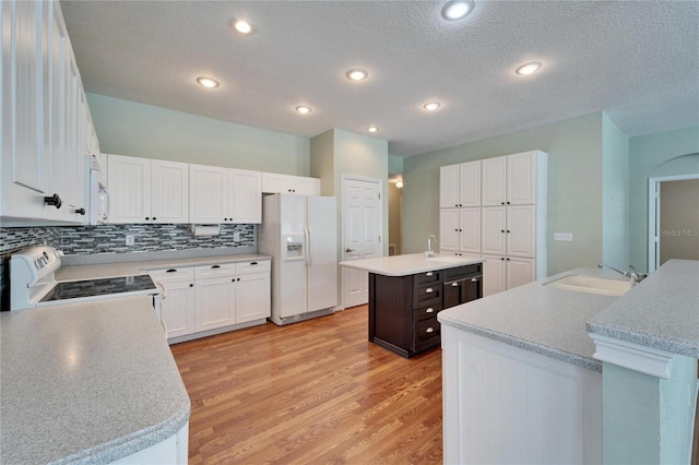 kitchen with a center island with sink, decorative backsplash, a sink, light wood-type flooring, and white appliances