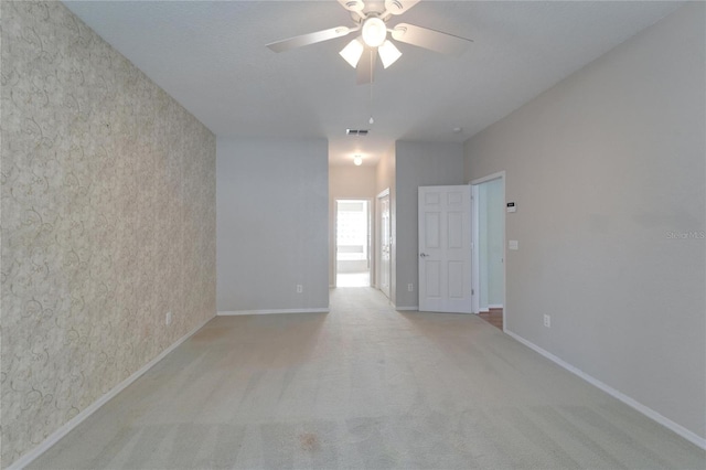 carpeted empty room featuring baseboards, visible vents, and a ceiling fan