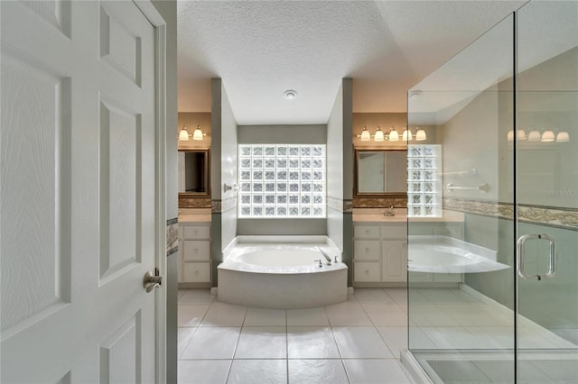 bathroom with a textured ceiling, two vanities, a shower stall, a bath, and tile patterned floors