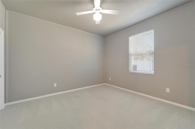 carpeted spare room featuring a ceiling fan and baseboards