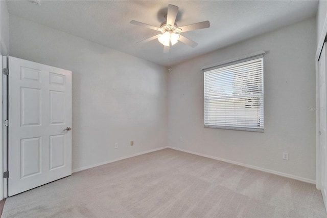 spare room featuring light carpet, baseboards, and a ceiling fan