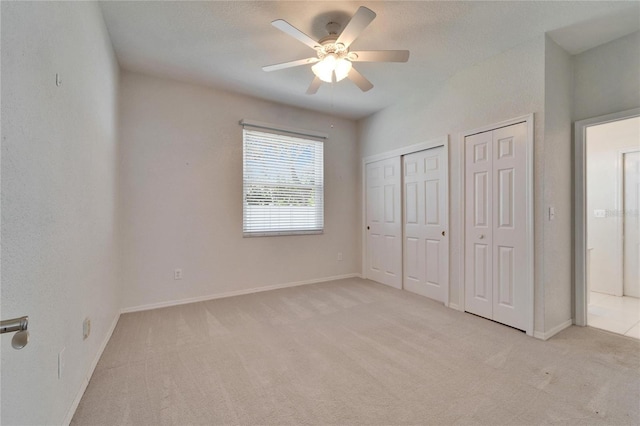 unfurnished bedroom with ceiling fan, baseboards, two closets, and light colored carpet