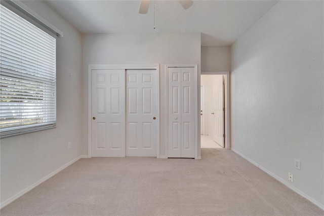 unfurnished bedroom with baseboards, multiple closets, a ceiling fan, and light colored carpet