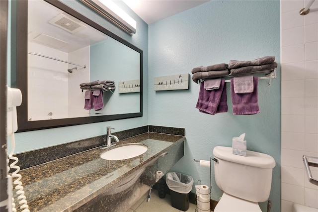 bathroom with a shower, visible vents, a textured wall, toilet, and a sink