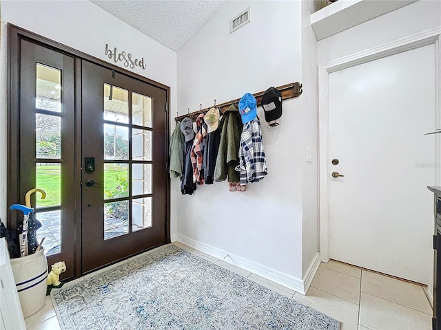 doorway with a textured ceiling, light tile patterned floors, visible vents, baseboards, and french doors