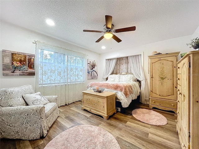 bedroom with a textured ceiling, ceiling fan, and light wood finished floors