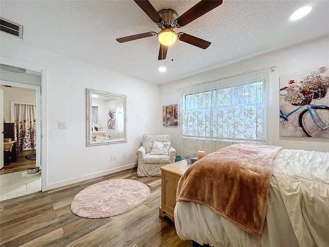 bedroom featuring visible vents, a textured ceiling, baseboards, and wood finished floors