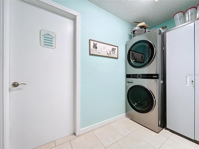 laundry area with stacked washer and dryer, laundry area, baseboards, tile patterned flooring, and a textured ceiling