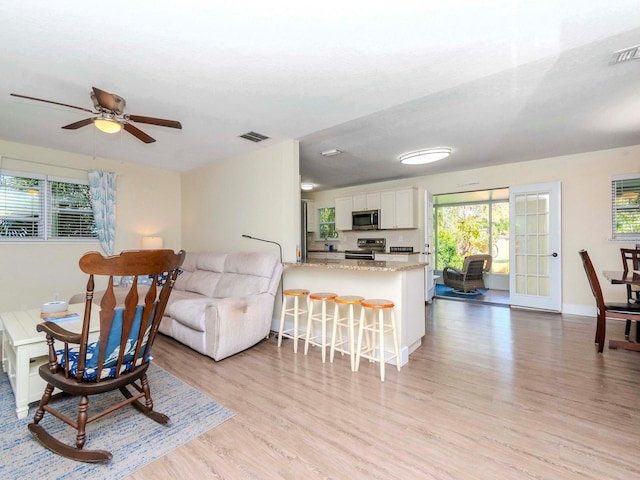 living area with light wood-style floors, baseboards, visible vents, and ceiling fan