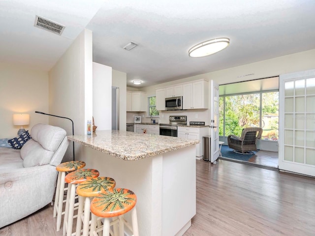 kitchen with light wood finished floors, visible vents, a peninsula, light stone countertops, and stainless steel appliances