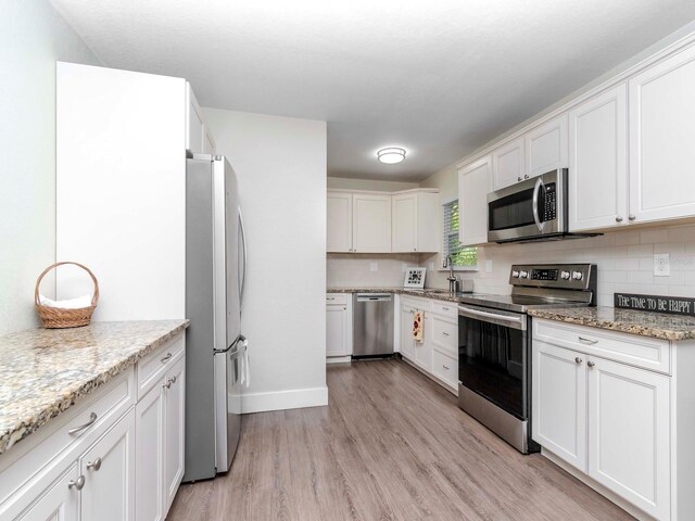 kitchen featuring light stone counters, stainless steel appliances, decorative backsplash, white cabinetry, and light wood-type flooring