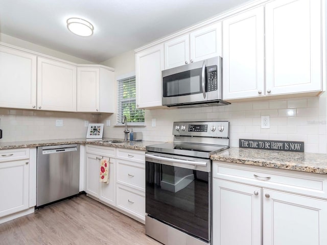 kitchen with tasteful backsplash, appliances with stainless steel finishes, light wood-type flooring, and white cabinets