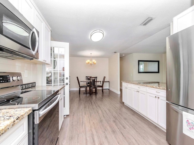 kitchen featuring stainless steel appliances, visible vents, white cabinetry, light wood-type flooring, and backsplash