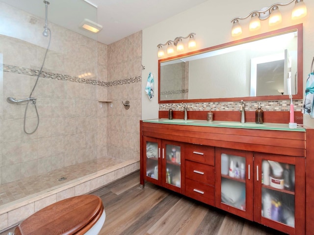 bathroom with double vanity, tasteful backsplash, wood finished floors, a walk in shower, and a sink