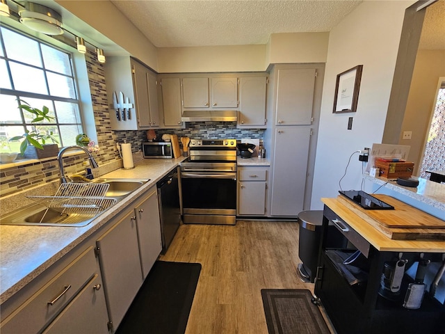 kitchen featuring gray cabinets, appliances with stainless steel finishes, a sink, light wood-type flooring, and under cabinet range hood