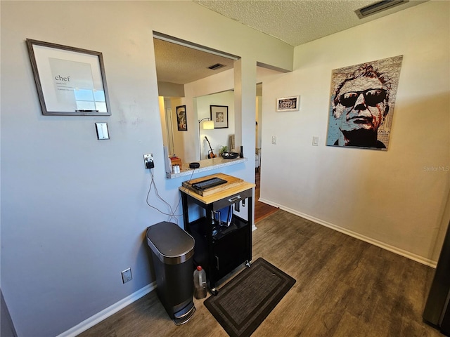 interior space with baseboards, a textured ceiling, visible vents, and wood finished floors