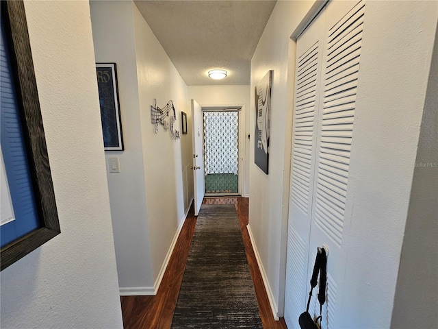 corridor featuring a textured ceiling, baseboards, and wood finished floors