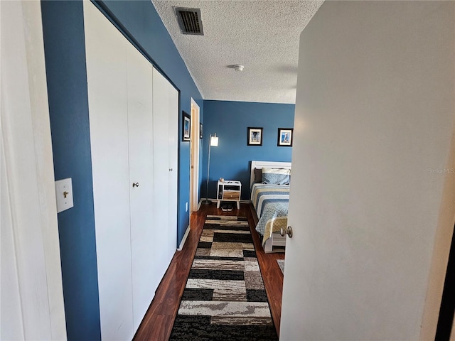 hall featuring baseboards, a textured ceiling, visible vents, and dark wood-type flooring