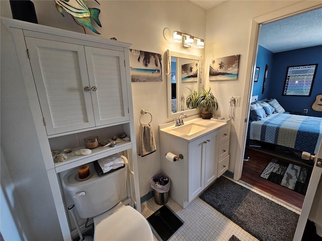 ensuite bathroom featuring connected bathroom, toilet, tile patterned flooring, a textured ceiling, and vanity