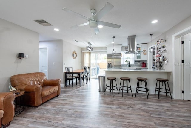 kitchen with stainless steel fridge, visible vents, a breakfast bar area, a peninsula, and island exhaust hood