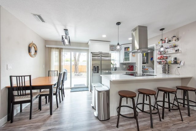 kitchen featuring island exhaust hood, visible vents, stainless steel fridge, a peninsula, and a kitchen bar