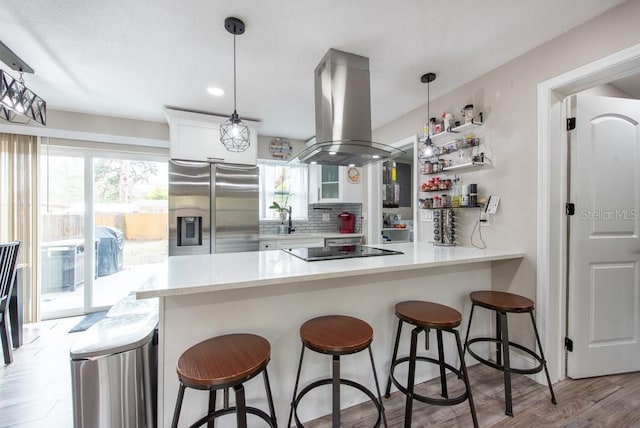 kitchen featuring decorative backsplash, a peninsula, island exhaust hood, white cabinetry, and stainless steel refrigerator with ice dispenser