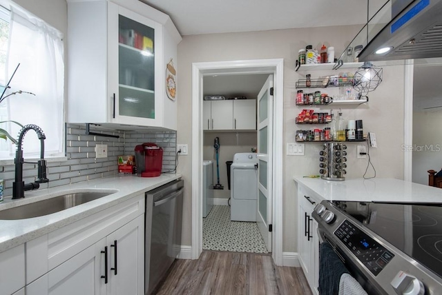 kitchen with appliances with stainless steel finishes, washer / dryer, white cabinetry, and a sink