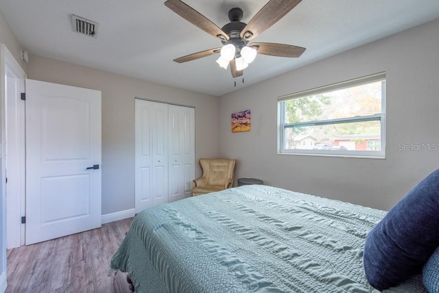 bedroom with a closet, visible vents, a ceiling fan, wood finished floors, and baseboards