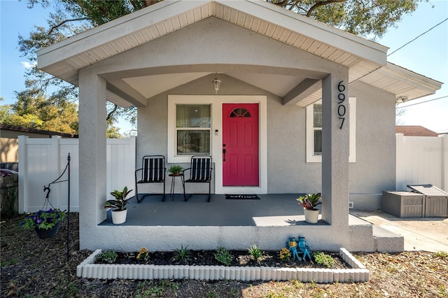 entrance to property with covered porch, fence, and stucco siding