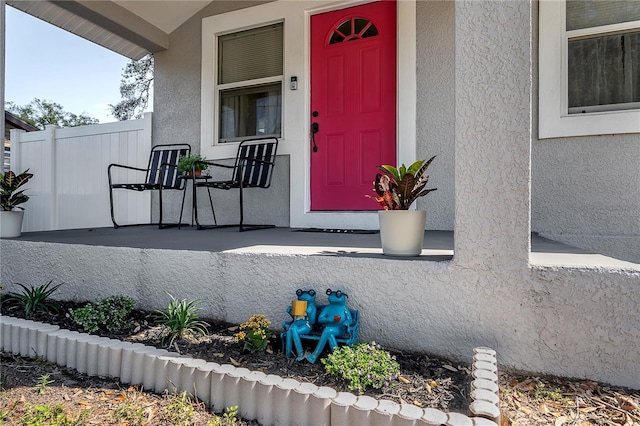 doorway to property featuring covered porch, fence, and stucco siding