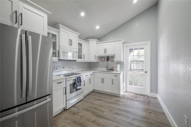 kitchen with light countertops, light wood-style flooring, vaulted ceiling, a sink, and white appliances