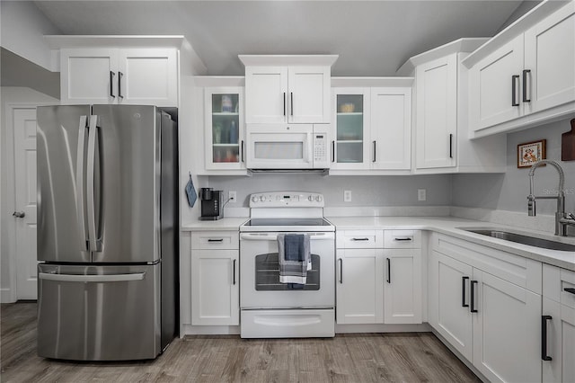 kitchen featuring white appliances, white cabinetry, light countertops, and a sink