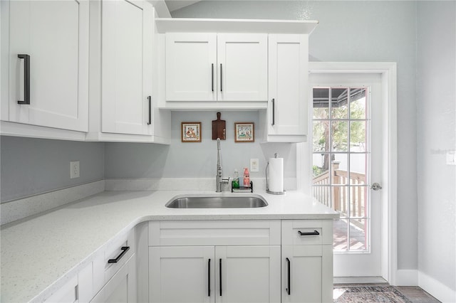 kitchen with baseboards, white cabinetry, light countertops, and a sink