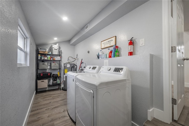 laundry room featuring electric water heater, laundry area, separate washer and dryer, wood finished floors, and baseboards