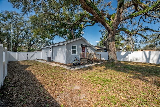 back of property with central AC, a yard, a fenced backyard, and a gate