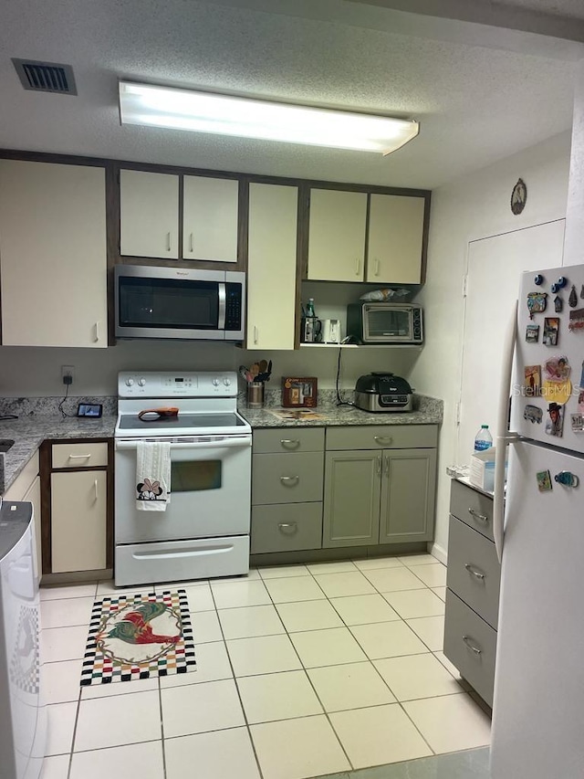 kitchen with a textured ceiling, light tile patterned flooring, white appliances, visible vents, and green cabinetry